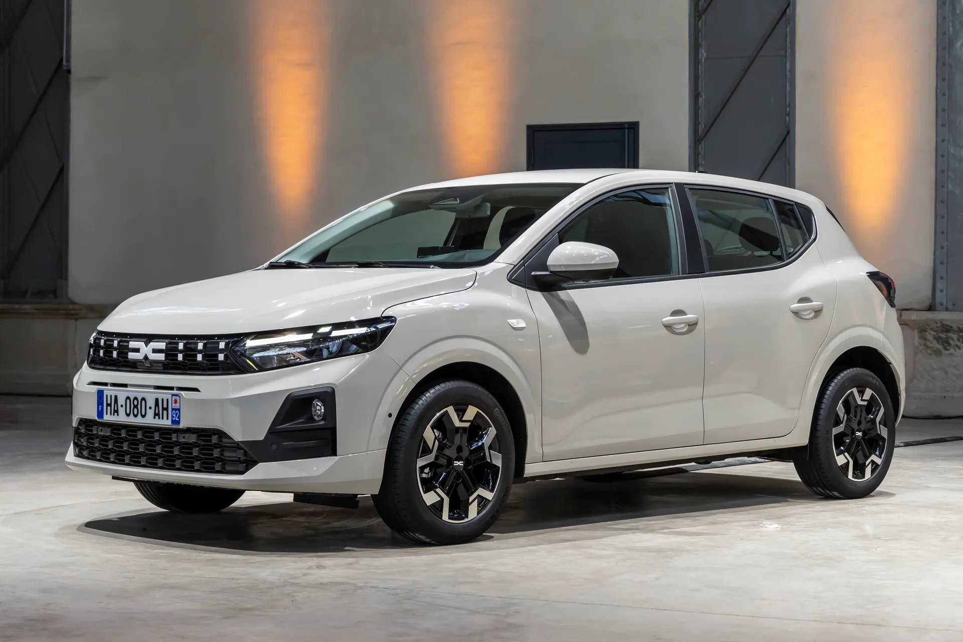 Hvid Dacia Sandero skråt forfra, parkeret i en lys hal med orange lys på væggen