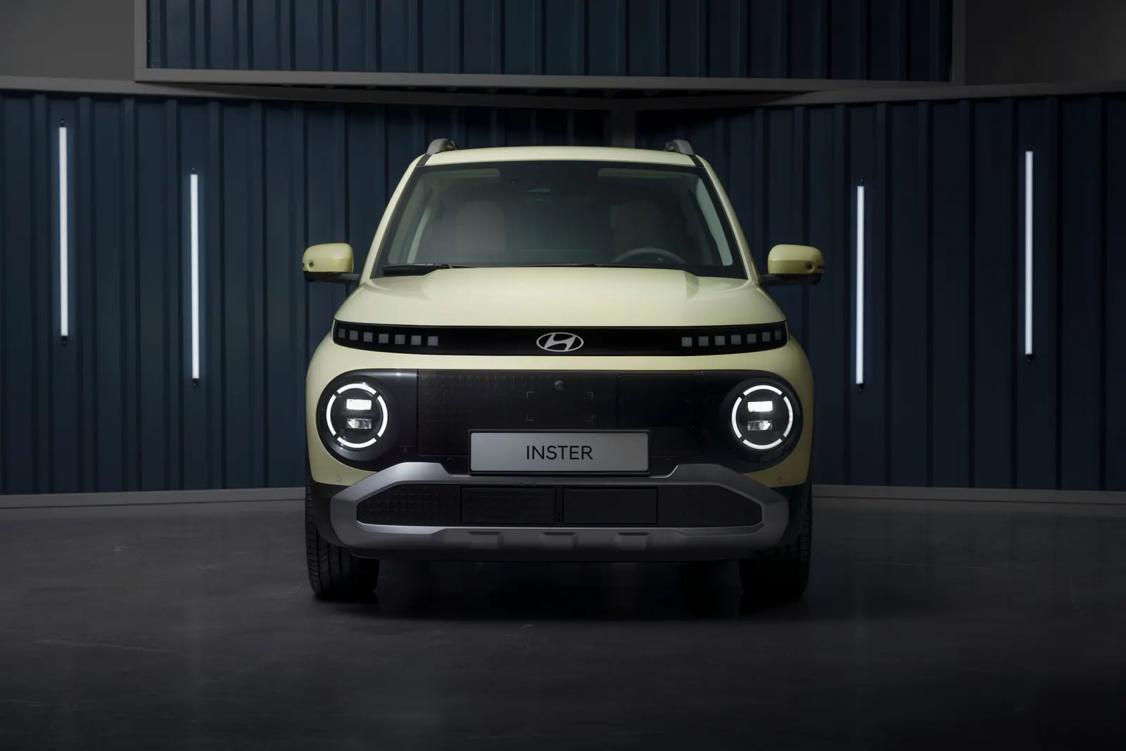Lysegrøn Hyundai Inster set skråt forfra i et mørkt studie