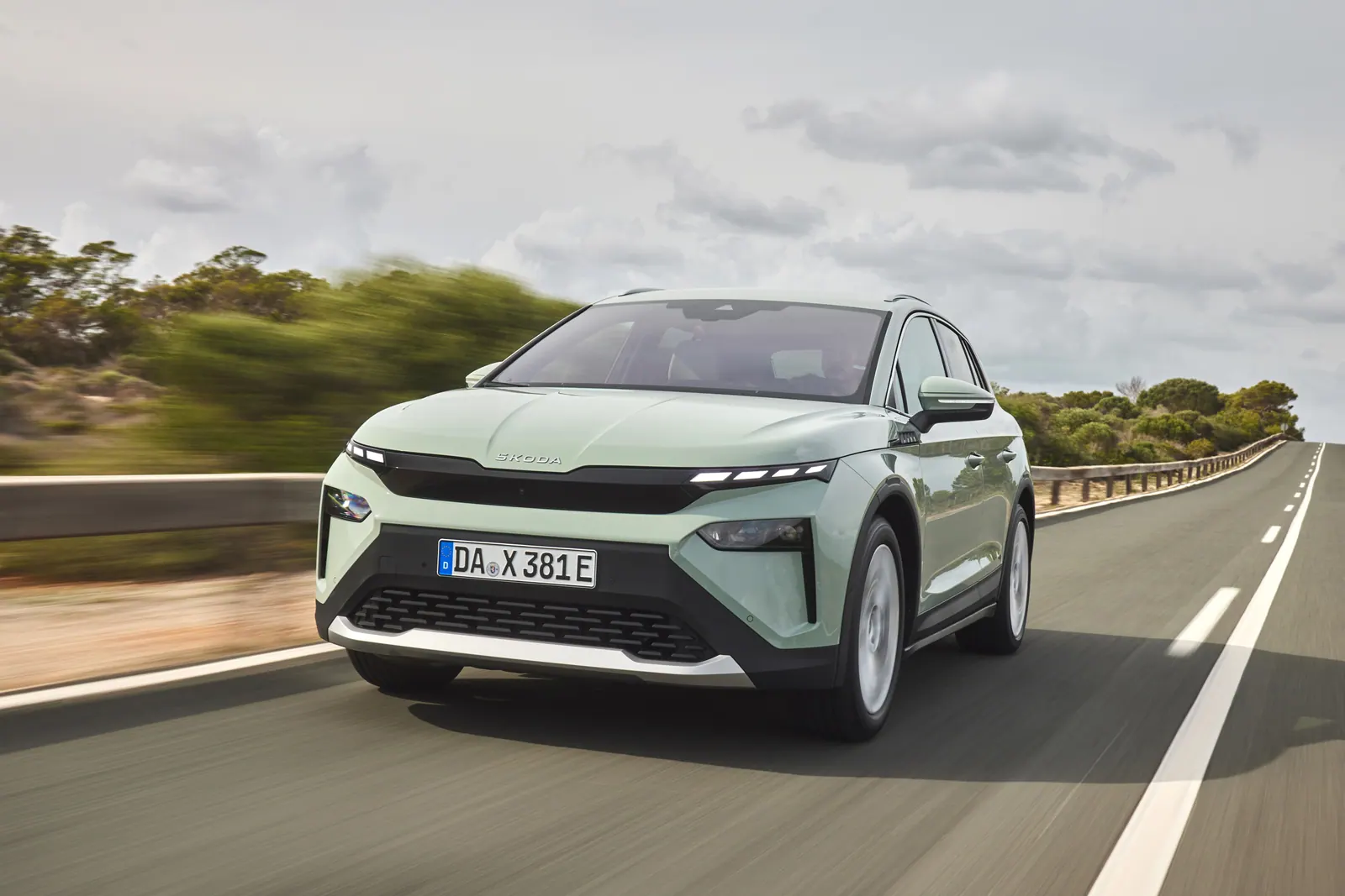 Lysegrøn Skoda Elroq parkeret på et udsigtspunkt over en bugt med bjerge i baggrunden