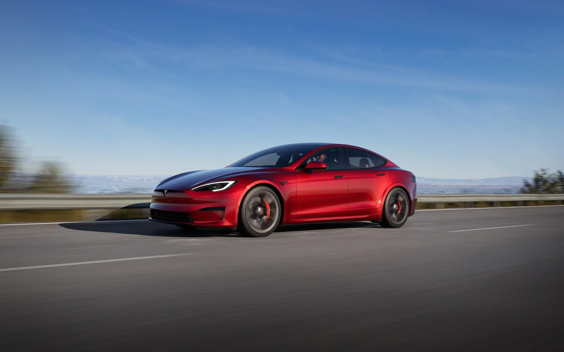 Rød Tesla Model S i fart på en kystvej
